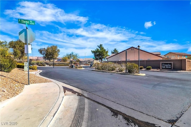 view of road with a gated entry, curbs, a gate, sidewalks, and street lights