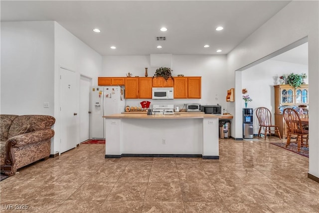 kitchen featuring a kitchen island with sink, white appliances, visible vents, light countertops, and brown cabinets