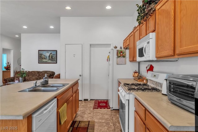 kitchen featuring recessed lighting, light countertops, a kitchen island with sink, a sink, and white appliances