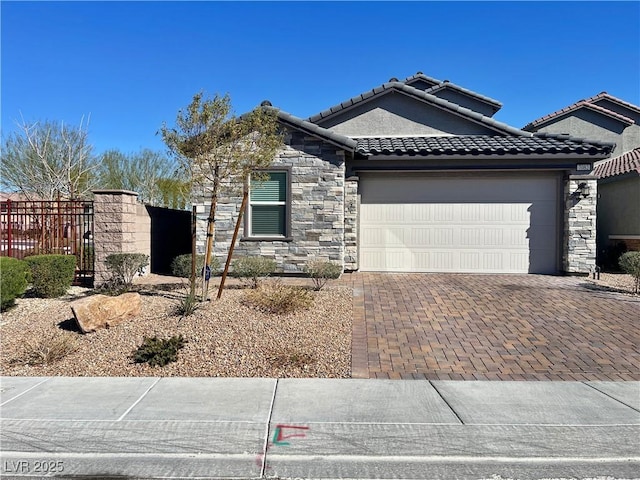 view of front of house featuring a garage, a tile roof, fence, stone siding, and decorative driveway