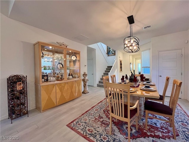 dining room with stairs, light wood finished floors, a chandelier, and visible vents