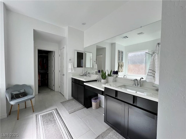 full bathroom with two vanities, a walk in closet, visible vents, and a sink