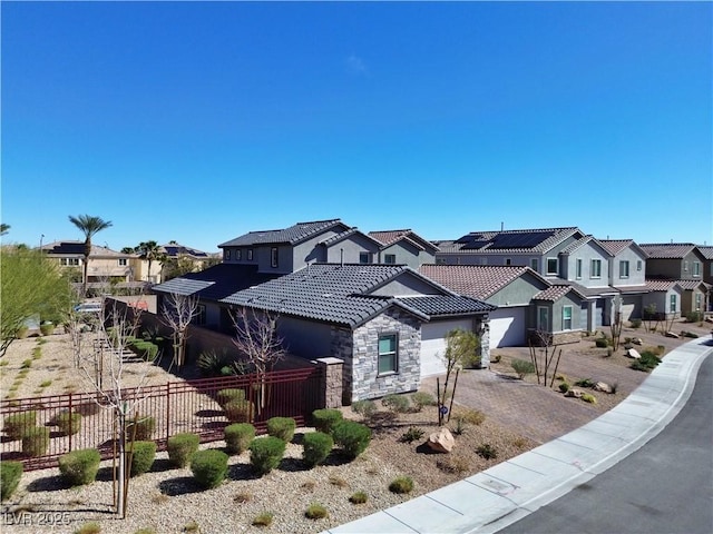 view of front of house featuring a tile roof, fence, a residential view, stone siding, and driveway