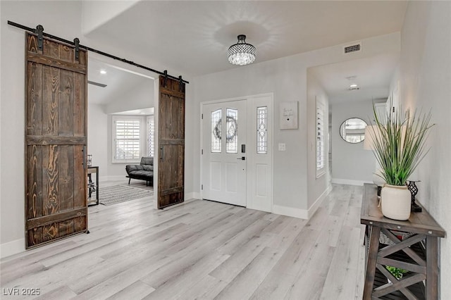 entryway featuring visible vents, light wood-style flooring, baseboards, and a barn door