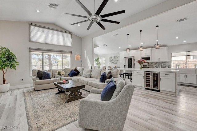 living area featuring light wood finished floors, high vaulted ceiling, wine cooler, and visible vents