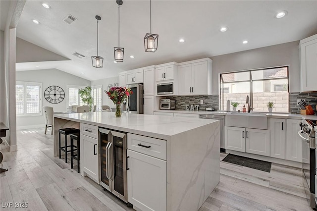 kitchen with wine cooler, stainless steel appliances, visible vents, vaulted ceiling, and a sink