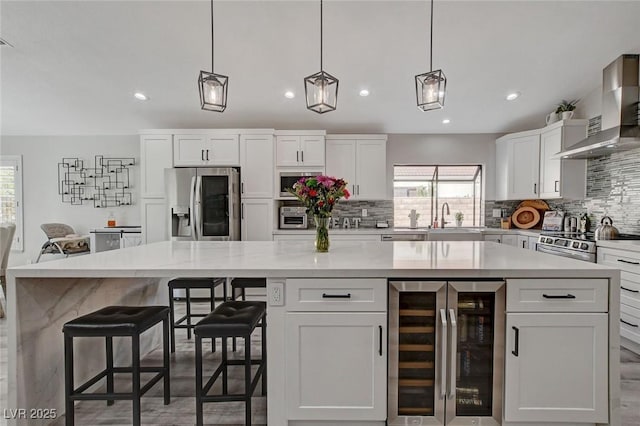 kitchen with appliances with stainless steel finishes, wine cooler, a healthy amount of sunlight, and wall chimney range hood