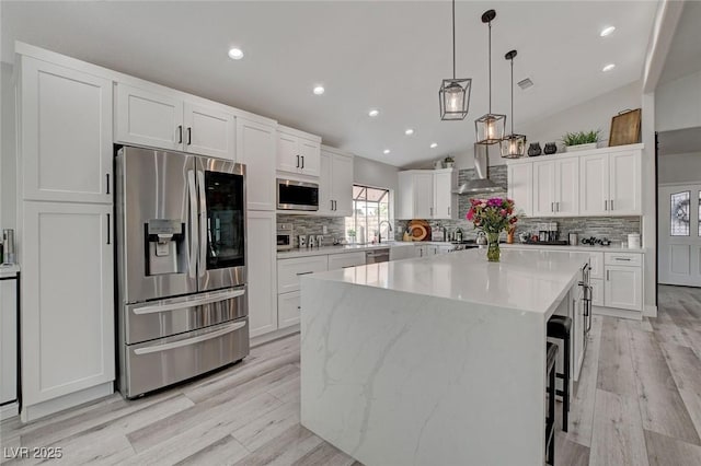 kitchen featuring stainless steel appliances, wall chimney exhaust hood, a center island, and white cabinets