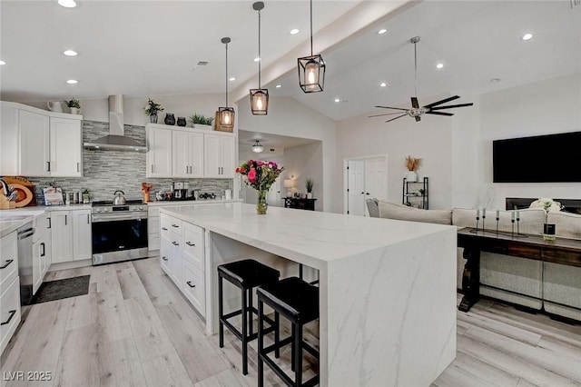 kitchen featuring a large island, stainless steel appliances, light wood-style flooring, decorative backsplash, and wall chimney range hood