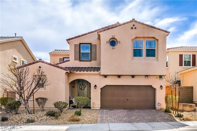 mediterranean / spanish-style house featuring a garage, decorative driveway, a tiled roof, and stucco siding