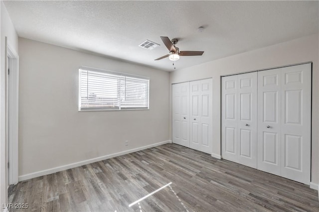 unfurnished bedroom with a textured ceiling, wood finished floors, visible vents, baseboards, and multiple closets