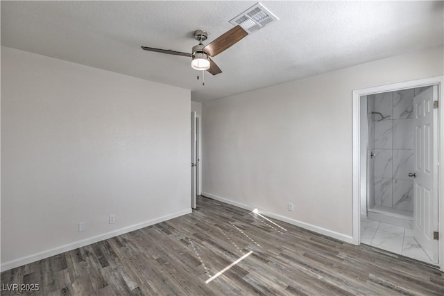 spare room featuring baseboards, visible vents, a ceiling fan, wood finished floors, and a textured ceiling