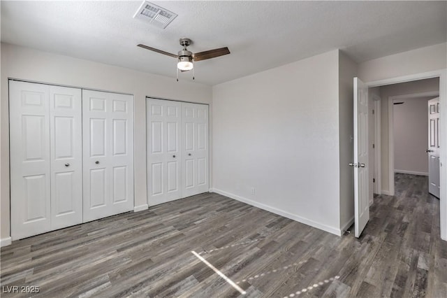 unfurnished bedroom with wood finished floors, a ceiling fan, baseboards, visible vents, and multiple closets