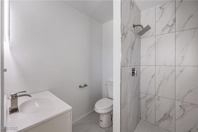 bathroom with baseboards, toilet, marble finish floor, a tile shower, and vanity