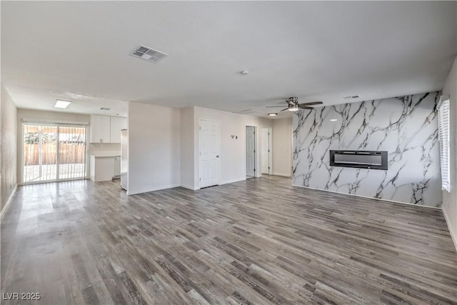 unfurnished living room featuring an accent wall, a fireplace, wood finished floors, visible vents, and a ceiling fan