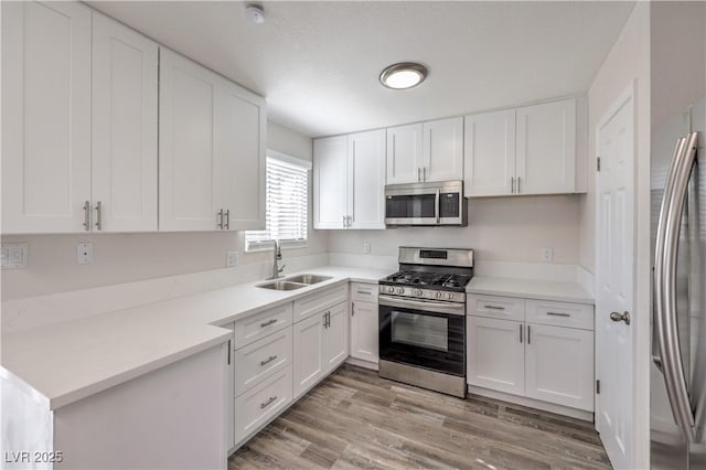 kitchen with light wood finished floors, white cabinets, stainless steel appliances, light countertops, and a sink