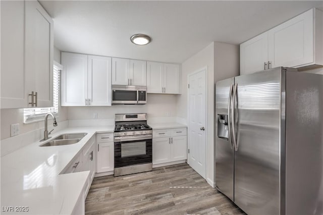 kitchen featuring appliances with stainless steel finishes, white cabinetry, a sink, and light wood-style flooring