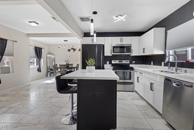 kitchen featuring visible vents, a kitchen island, a sink, light countertops, and appliances with stainless steel finishes