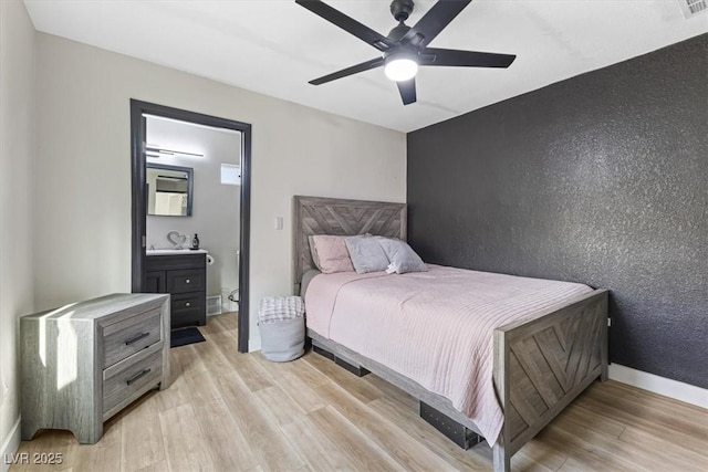 bedroom with ensuite bath, baseboards, light wood finished floors, and ceiling fan