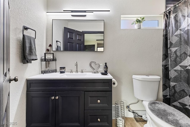 bathroom with toilet, vanity, a textured wall, and wood finished floors