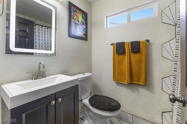 bathroom with toilet, marble finish floor, vanity, and a textured wall