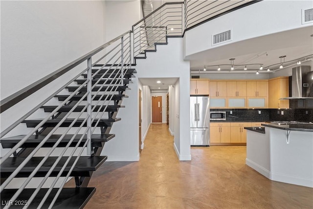 kitchen with stainless steel appliances, dark countertops, visible vents, light brown cabinets, and wall chimney exhaust hood