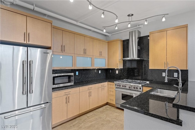 kitchen featuring tasteful backsplash, appliances with stainless steel finishes, a sink, dark stone counters, and wall chimney exhaust hood