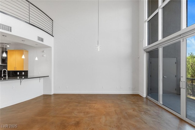 interior space with a towering ceiling, baseboards, finished concrete flooring, and visible vents