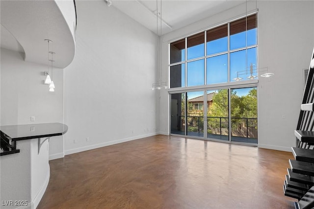 unfurnished living room with a high ceiling, finished concrete floors, and baseboards