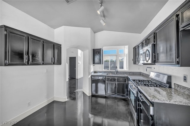 kitchen featuring baseboards, arched walkways, lofted ceiling, stainless steel appliances, and a sink