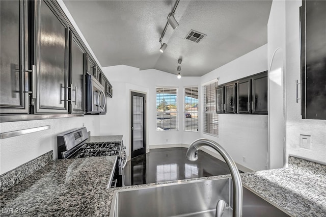 kitchen with a textured ceiling, lofted ceiling, stainless steel appliances, a sink, and visible vents