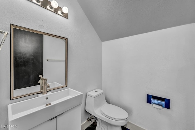 bathroom featuring lofted ceiling, a textured wall, vanity, and toilet