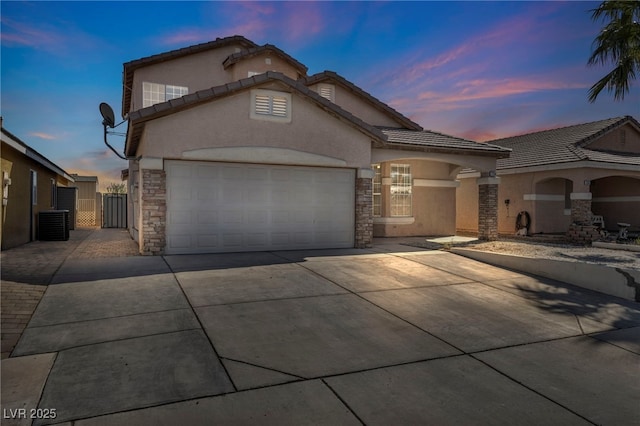 view of front facade with driveway, a garage, stone siding, a gate, and stucco siding