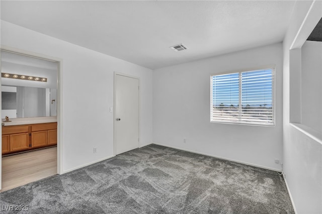 unfurnished bedroom with visible vents, connected bathroom, a sink, and carpet flooring