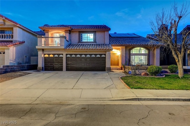 mediterranean / spanish-style house featuring a garage, concrete driveway, a balcony, roof mounted solar panels, and stucco siding