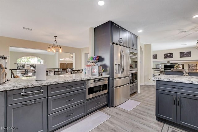 kitchen with light stone counters, a peninsula, visible vents, stainless steel refrigerator with ice dispenser, and built in microwave