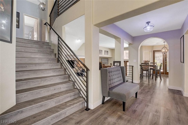 staircase with arched walkways, baseboards, and wood finished floors