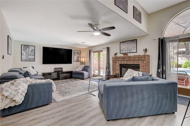 living room with a brick fireplace, ceiling fan, and light wood-style flooring