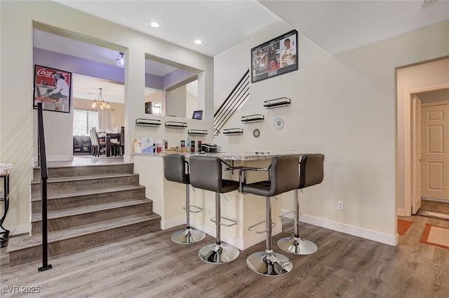 bar featuring a notable chandelier, baseboards, stairway, and wood finished floors