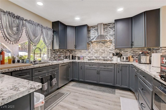 kitchen with light wood finished floors, decorative backsplash, appliances with stainless steel finishes, a sink, and wall chimney range hood