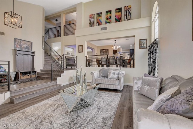 living room featuring a chandelier, wood finished floors, visible vents, and stairs