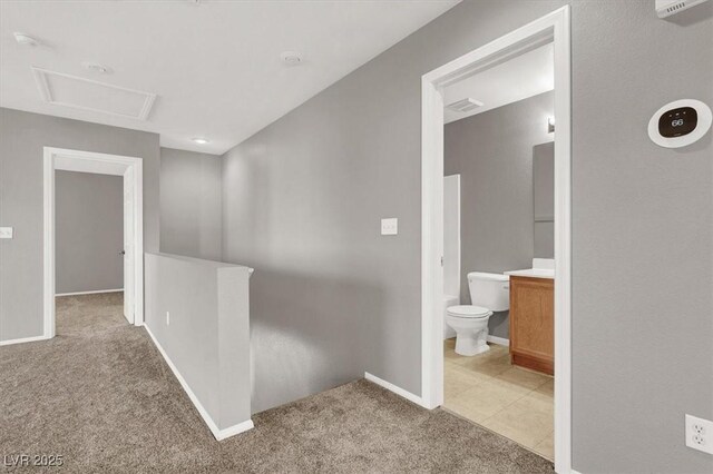 hall featuring light tile patterned flooring, light colored carpet, visible vents, baseboards, and attic access