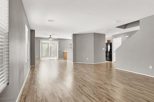 unfurnished living room featuring a ceiling fan, wood finished floors, visible vents, and baseboards