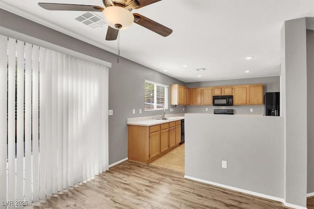 kitchen with a sink, visible vents, light countertops, light wood-type flooring, and black appliances