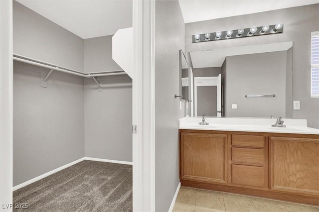 bathroom featuring double vanity, a sink, a walk in closet, and baseboards