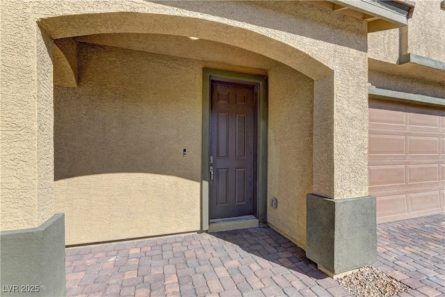 entrance to property featuring a garage and stucco siding