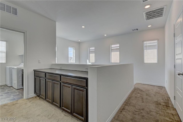 kitchen featuring light carpet, washer and clothes dryer, and visible vents