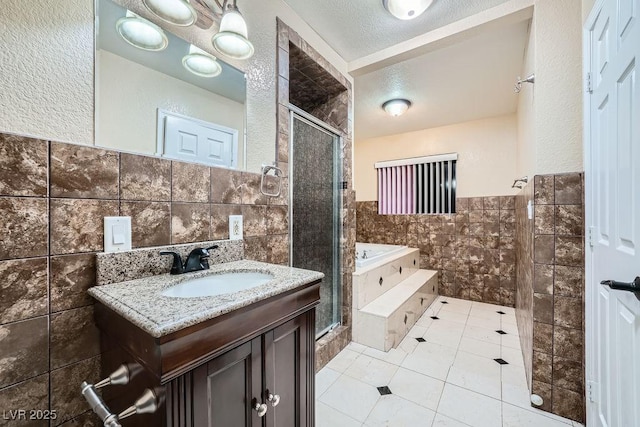 full bath with a textured ceiling, a garden tub, vanity, tile walls, and a stall shower