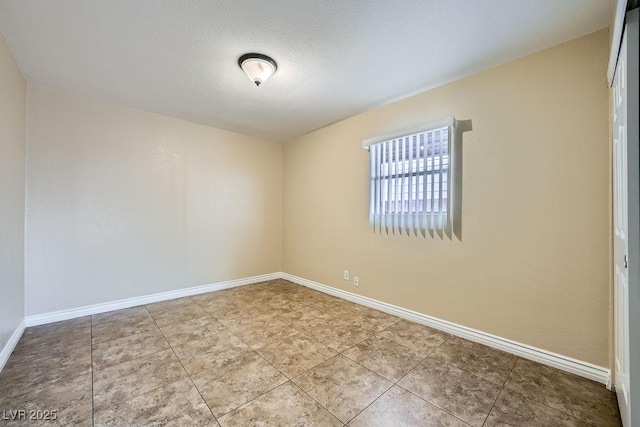 tiled spare room featuring a textured ceiling and baseboards