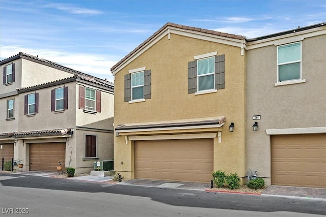 townhome / multi-family property with a garage, central AC unit, and stucco siding